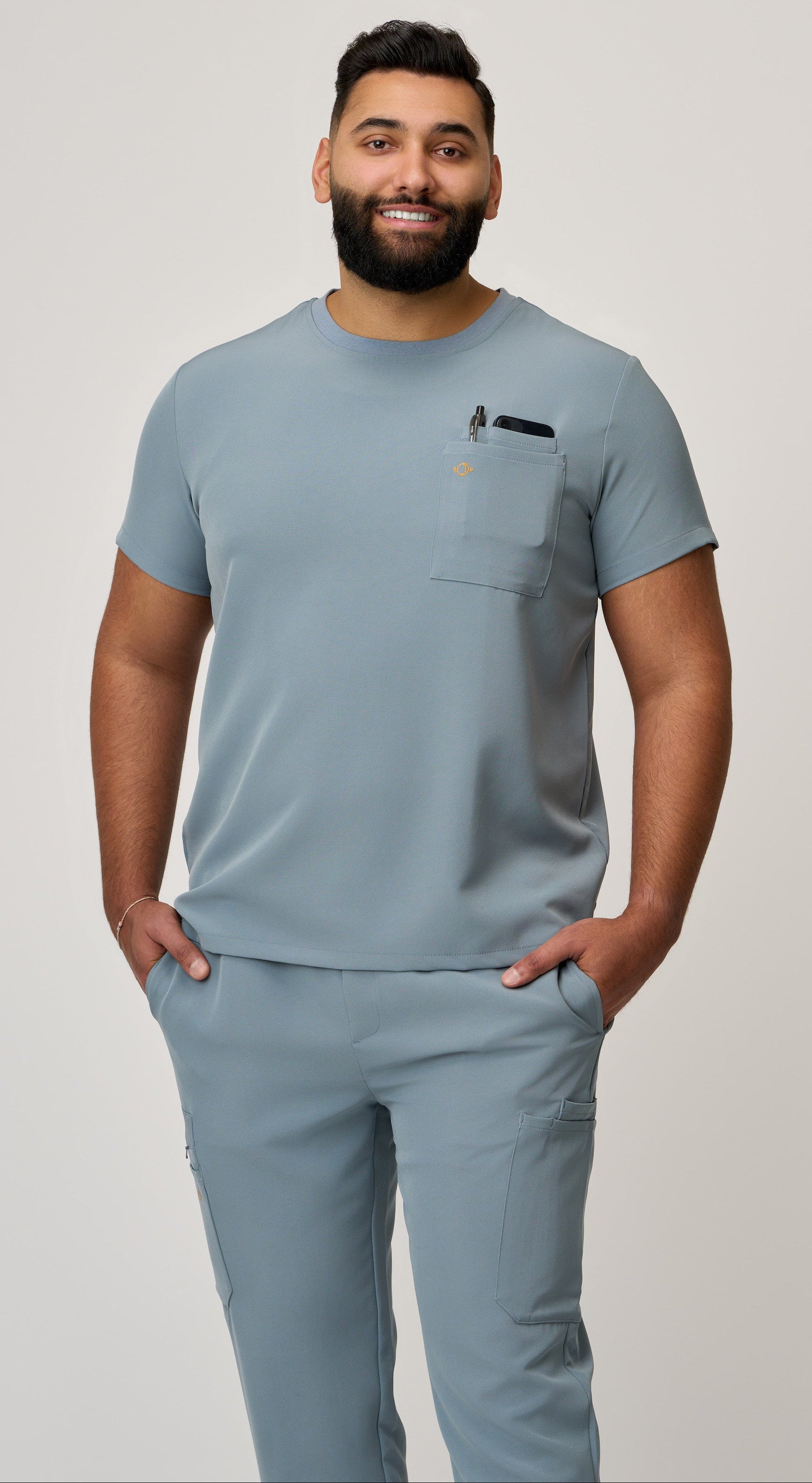 A person wearing a light blue scrub top with a crewneck and two pockets, one of which has a pen in it.